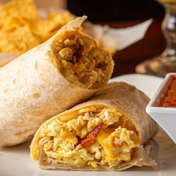 Two breakfast burritos filled with scrambled eggs, cheese, and bacon, served with salsa and tortilla chips.