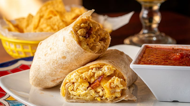 Two breakfast burritos filled with scrambled eggs, cheese, and bacon, served with salsa and tortilla chips.