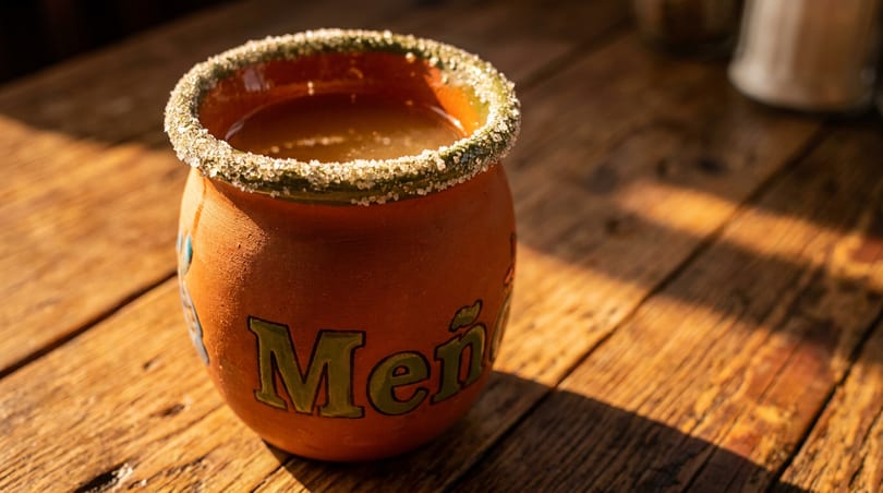 A clay mug with "Meño" written on it, filled with a drink and a sugar-rimmed edge.
