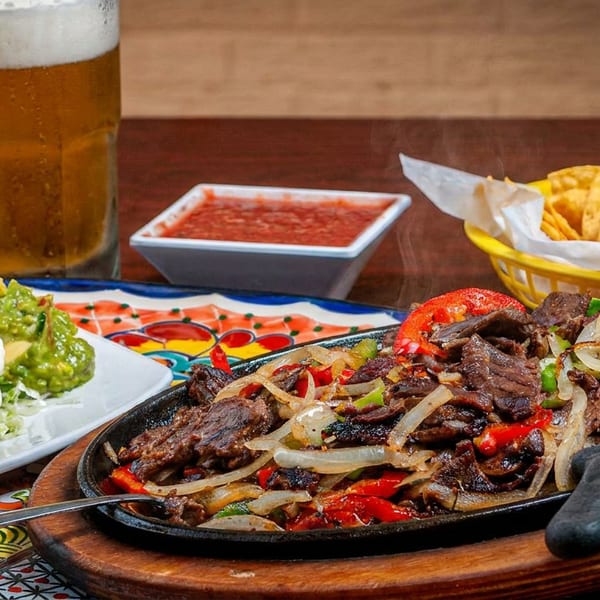 Sizzling steak fajitas with onions and peppers, served with beans, guacamole, salsa, and tortilla chips.