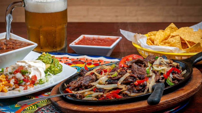 Sizzling beef fajitas with onions and peppers, served with beans, guacamole, salsa, and tortilla chips.