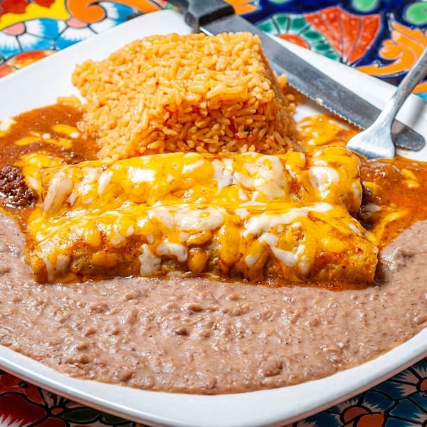 Cheesy enchiladas with red sauce, refried beans, and rice on a white plate with a colorful placemat.
