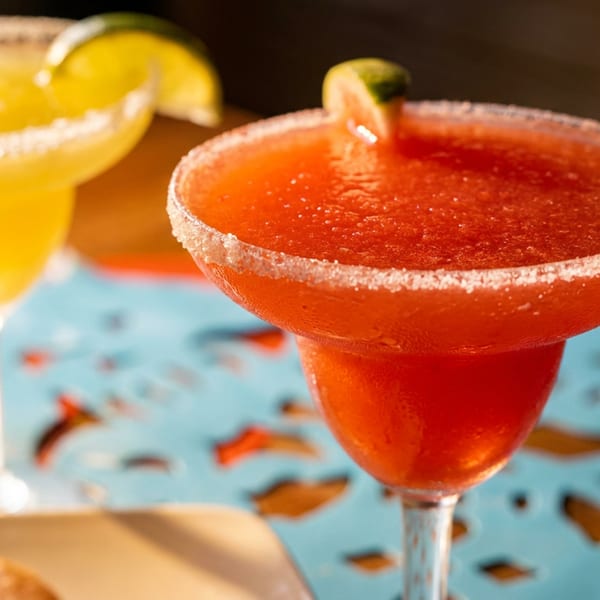 Two vibrant margaritas, one red and one yellow, with salted rims and lime garnishes on a blue placemat.