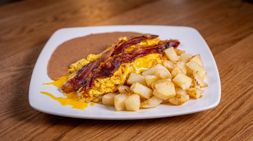Scrambled eggs with melted cheese and bacon, served with home fries and refried beans.