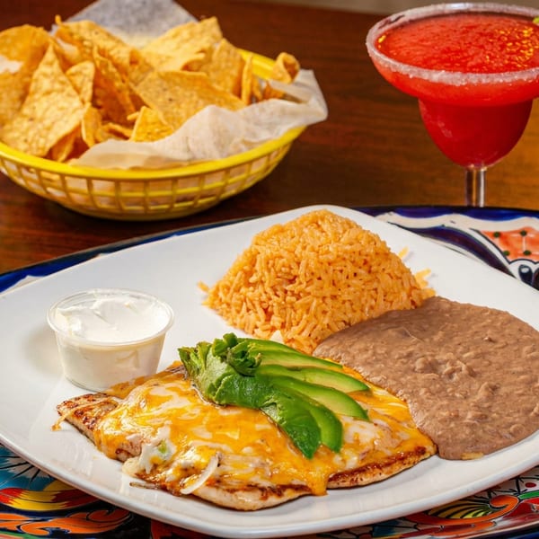 Cheesy chicken with avocado, rice, and beans, served with chips, salsa, and a margarita.