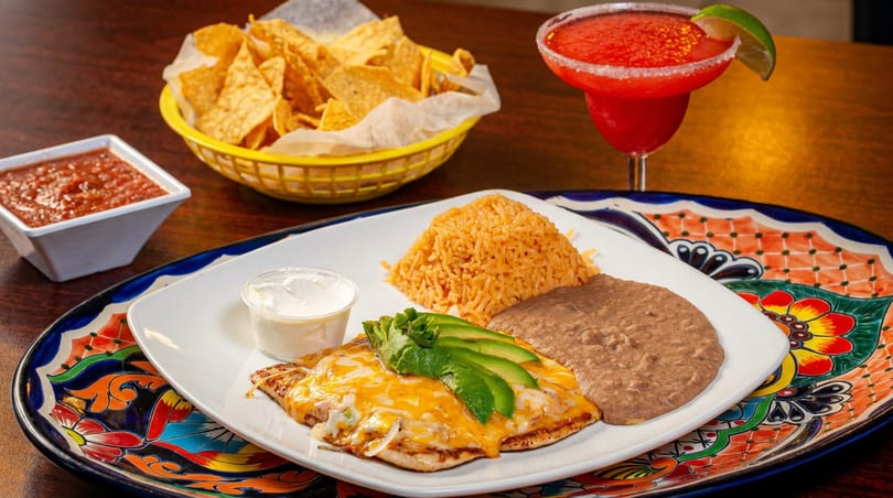 Cheesy chicken with avocado, rice, and beans, served with chips, salsa, and a margarita.