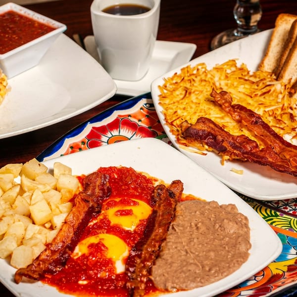 A table spread with various breakfast dishes, including burritos, eggs, bacon, hash browns, and coffee.