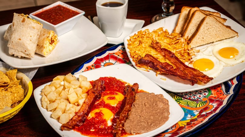 Three plates of breakfast food, including burritos, eggs, bacon, hash browns, and coffee.