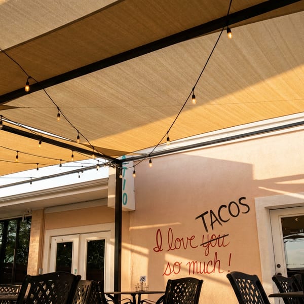 Outdoor patio with string lights under a beige canopy, and a wall with "TACOS I love you so much!" written on it.